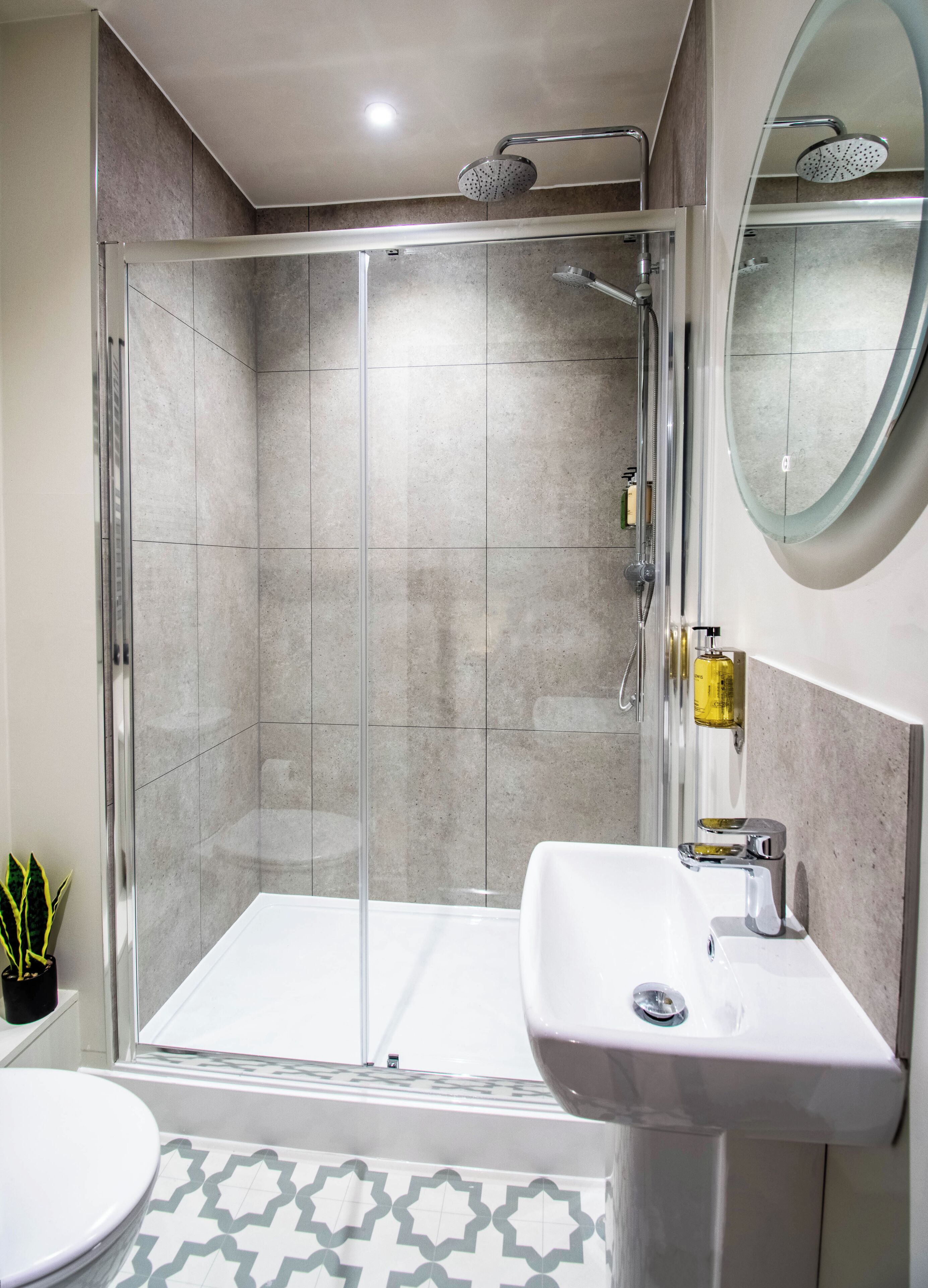 Un baño moderno con cabina de ducha de vidrio, un lavabo blanco y un espejo grande.