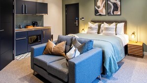A modern bedroom with a bed, a sofa, a kitchenette, and artwork on the wall. - Thetford Hive (Thetford)