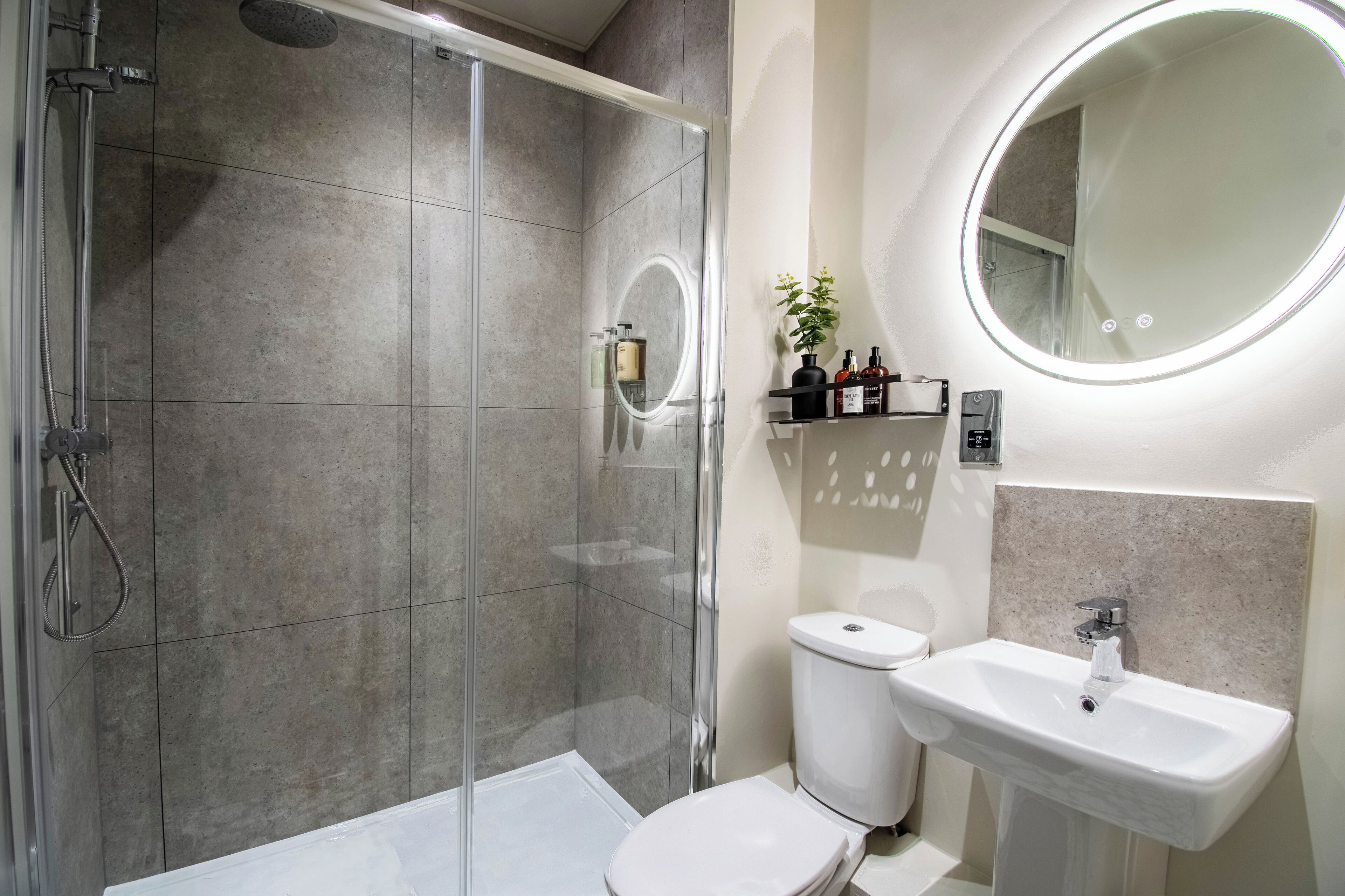 A modern bathroom with a glass-enclosed shower, a white toilet, and a sink with a mirror above it.