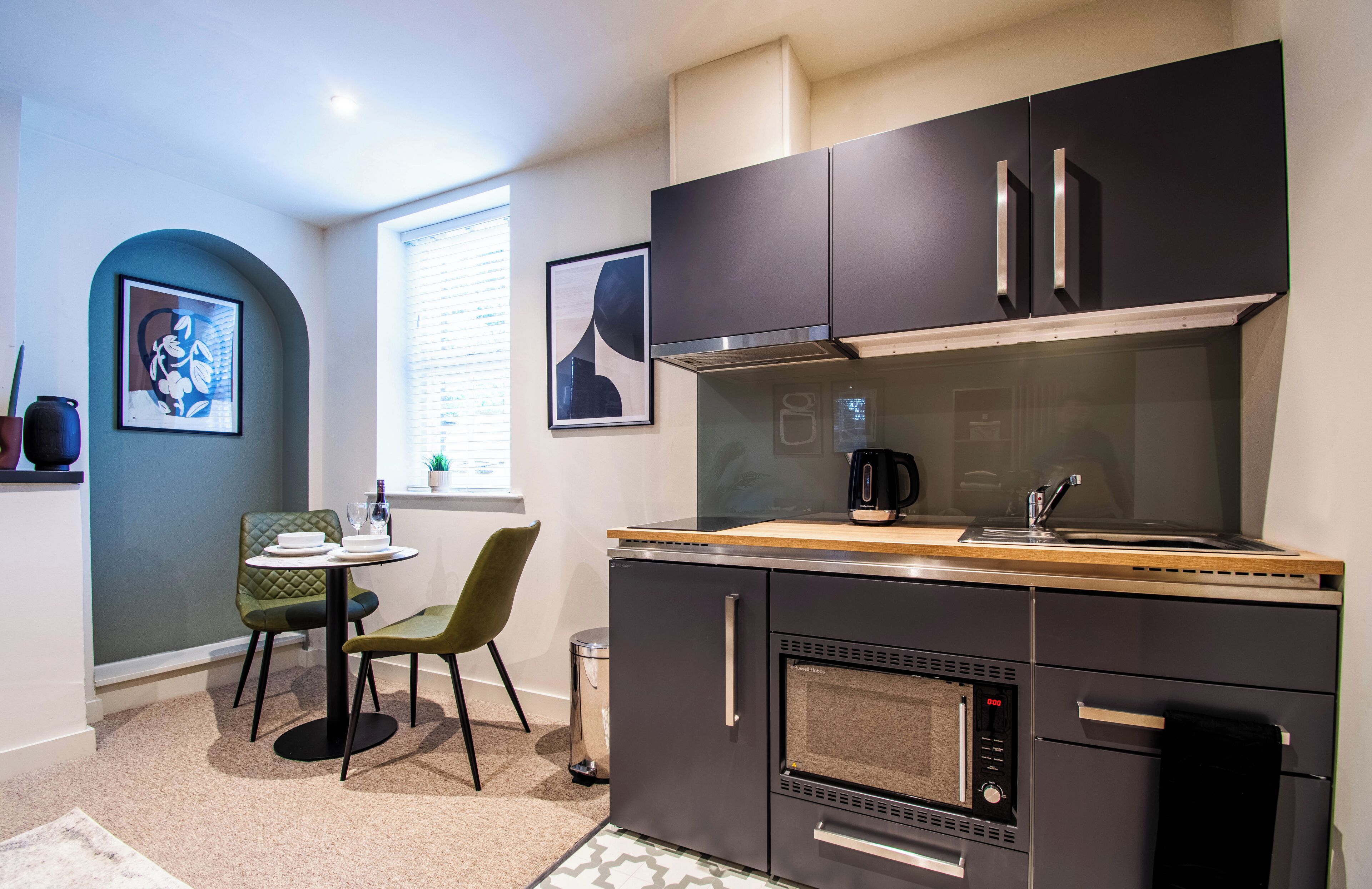 Una cocina compacta con electrodomésticos modernos, una zona de comedor con una pequeña mesa y sillas, y obras de arte en las paredes.