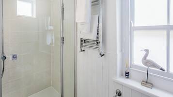 A bathroom with a glass-enclosed shower, a white tiled wall, a towel rack, and a window with a bird outside.