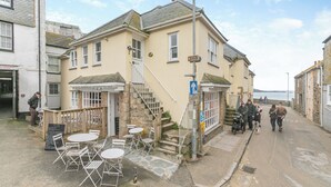 A building with a staircase leading to the entrance, outdoor seating with tables and chairs, and a sign indicating a museum nearby. - 2 bedroom accommodation in St Ives (St Ives)