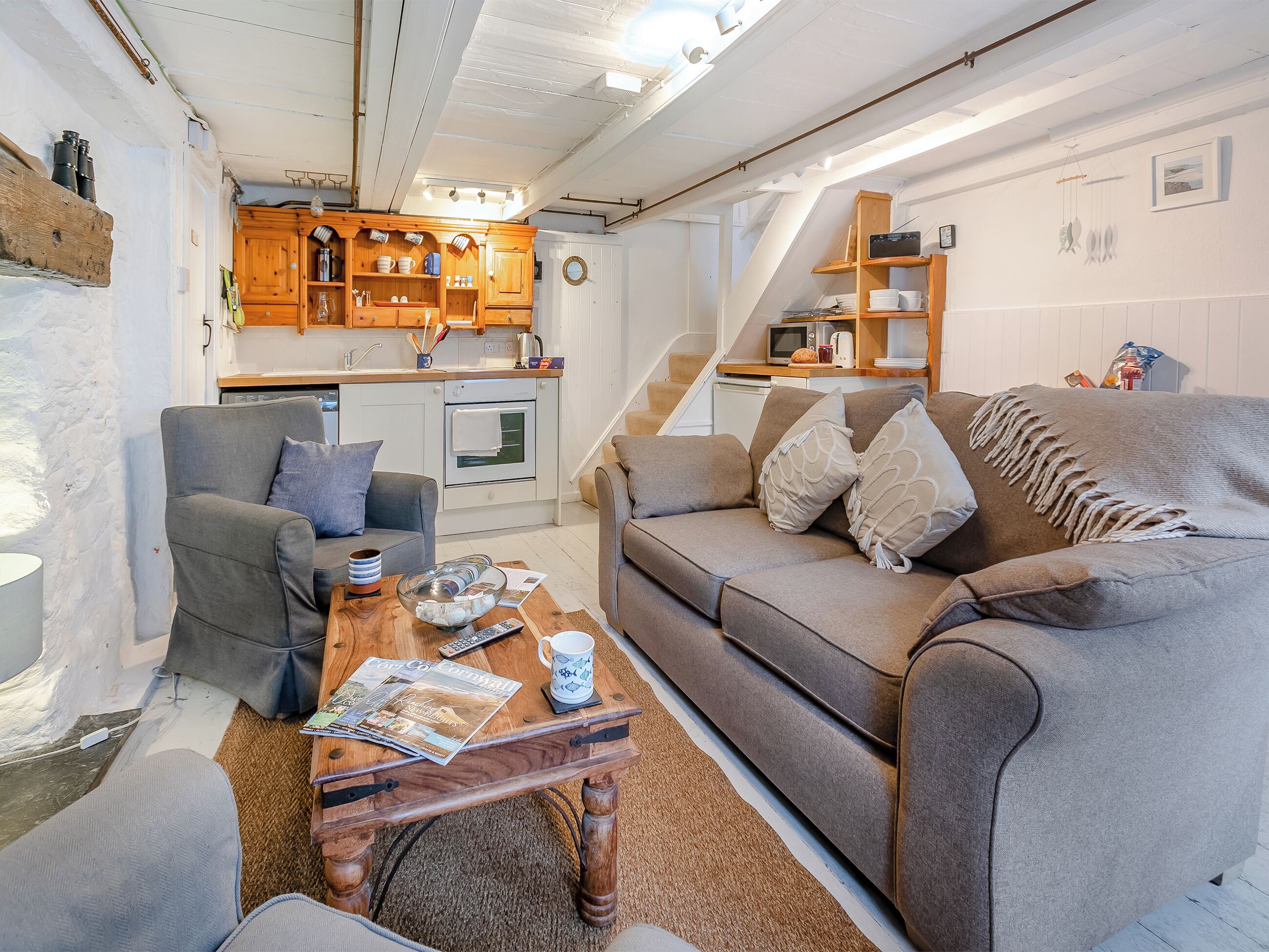 A cozy living room with a sofa, armchairs, a coffee table, and a kitchen area with wooden cabinets and a microwave.