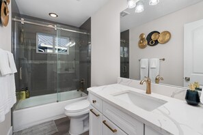 Un baño moderno con ducha envuelta en vidrio, inodoro blanco, tocador con lavamanos y un espejo grande.