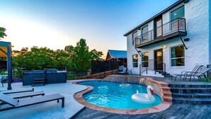 Una casa moderna con piscina, mobiliario exterior y una escalera que lleva a un balcón.