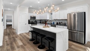 Una cocina moderna con armarios blancos, un refrigerador de acero inoxidable e una isla de mármol con taburetes de bar.