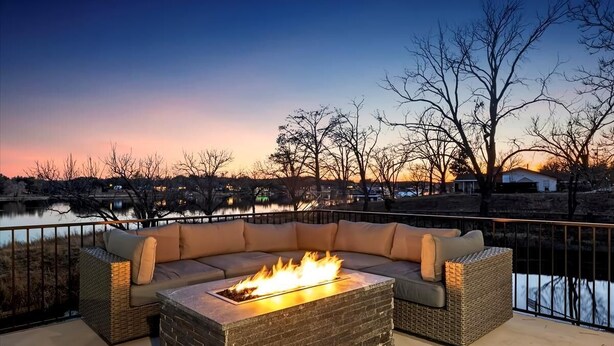 Una chimenea con un sofá y cojines en un patio con vista a un cuerpo de agua.