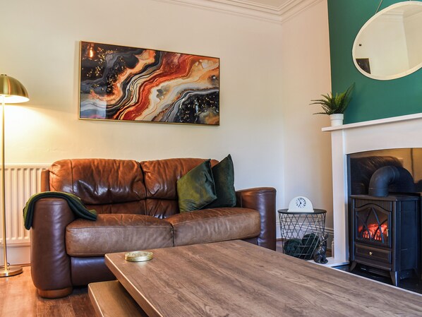 Un salon avec un canapé en cuir marron, une table basse en bois, une cheminée et un tableau abstrait aux couleurs vives accroché au mur.