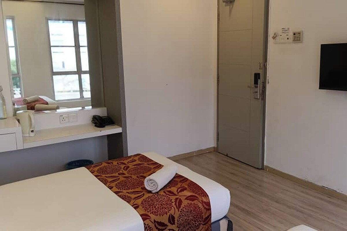 Een kamer met een bed, een klein tafeltje met een handdoek, een spiegel en een televisie aan de muur.