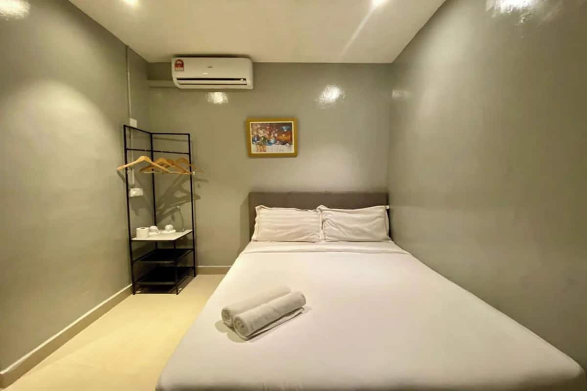A hotel room with a bed, a wall-mounted air conditioner, a shelf with toiletries, and a framed picture on the wall.