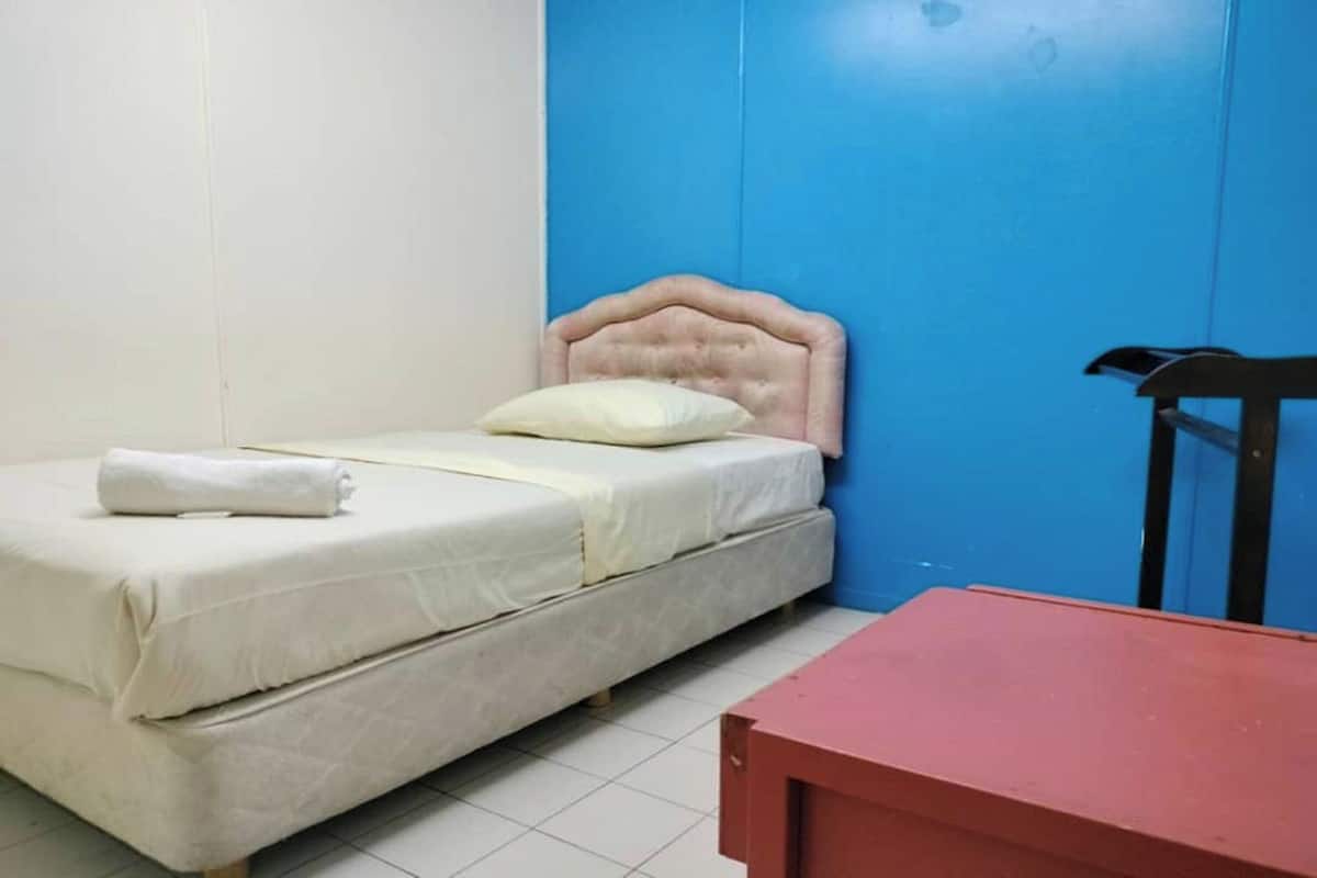 A single bed with a headboard, a small table, and a chair in a room with blue and white walls.