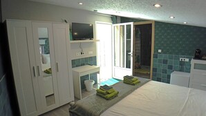 A bedroom with a bed, a wardrobe, a television, a bathroom with a shower, and a sink.