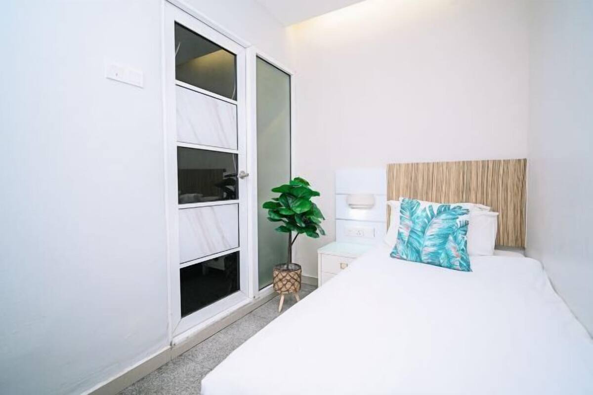 A bedroom with a bed, a bedside table, a lamp, a plant, and a sliding door.