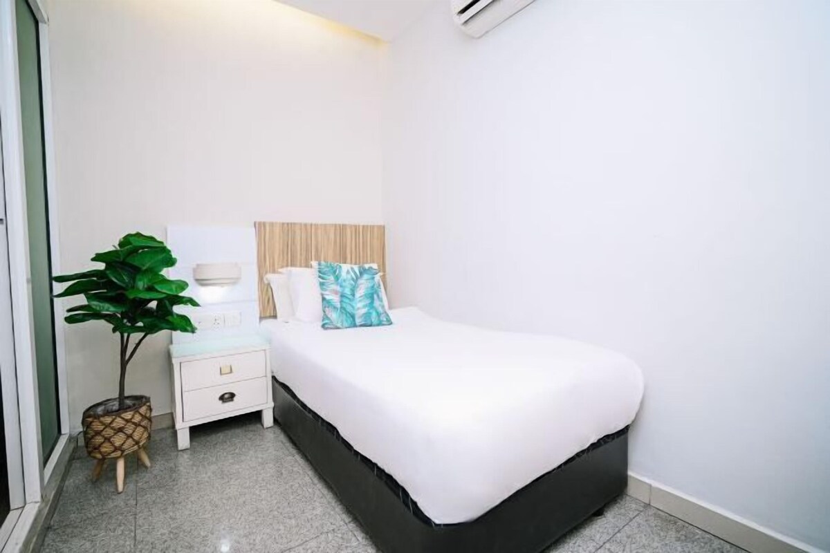 A bedroom with a bed, bedside table, lamp, and a potted plant.