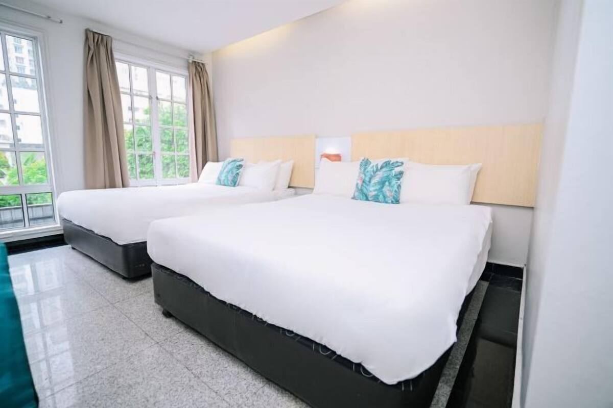 A hotel room with two beds, a large window with curtains, and a view of greenery outside.