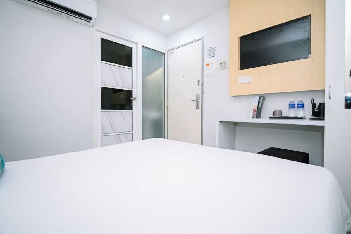 A hotel room with a bed, a TV mounted on the wall, a small desk with a chair, and a door leading to a closet.