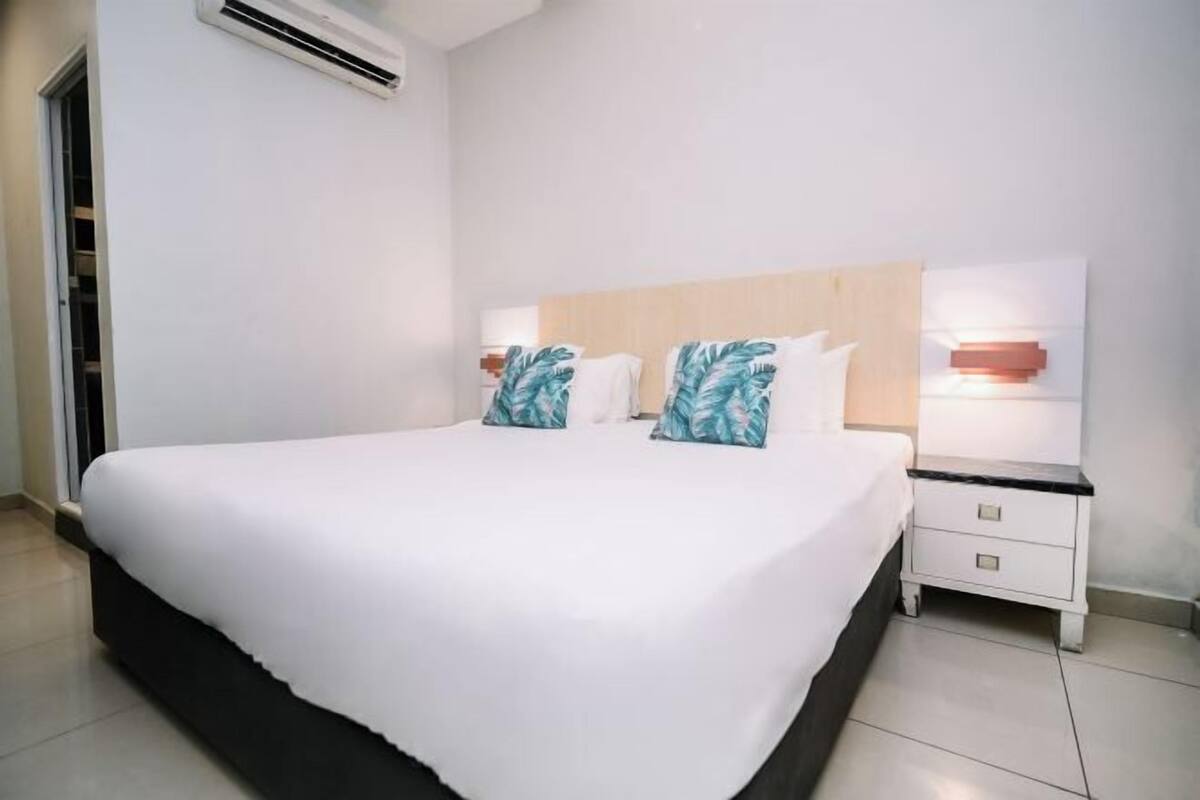 A hotel room with a large bed, two bedside tables, a nightstand, and a wall-mounted air conditioning unit.