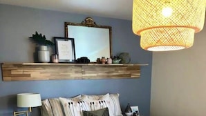 A bedroom with a bed, bedside tables, a lamp, a hanging light fixture, and a shelf with decorative items. - Caitlin's Cottage - Peaceful 2BR Retreat in North Marion (Marion)