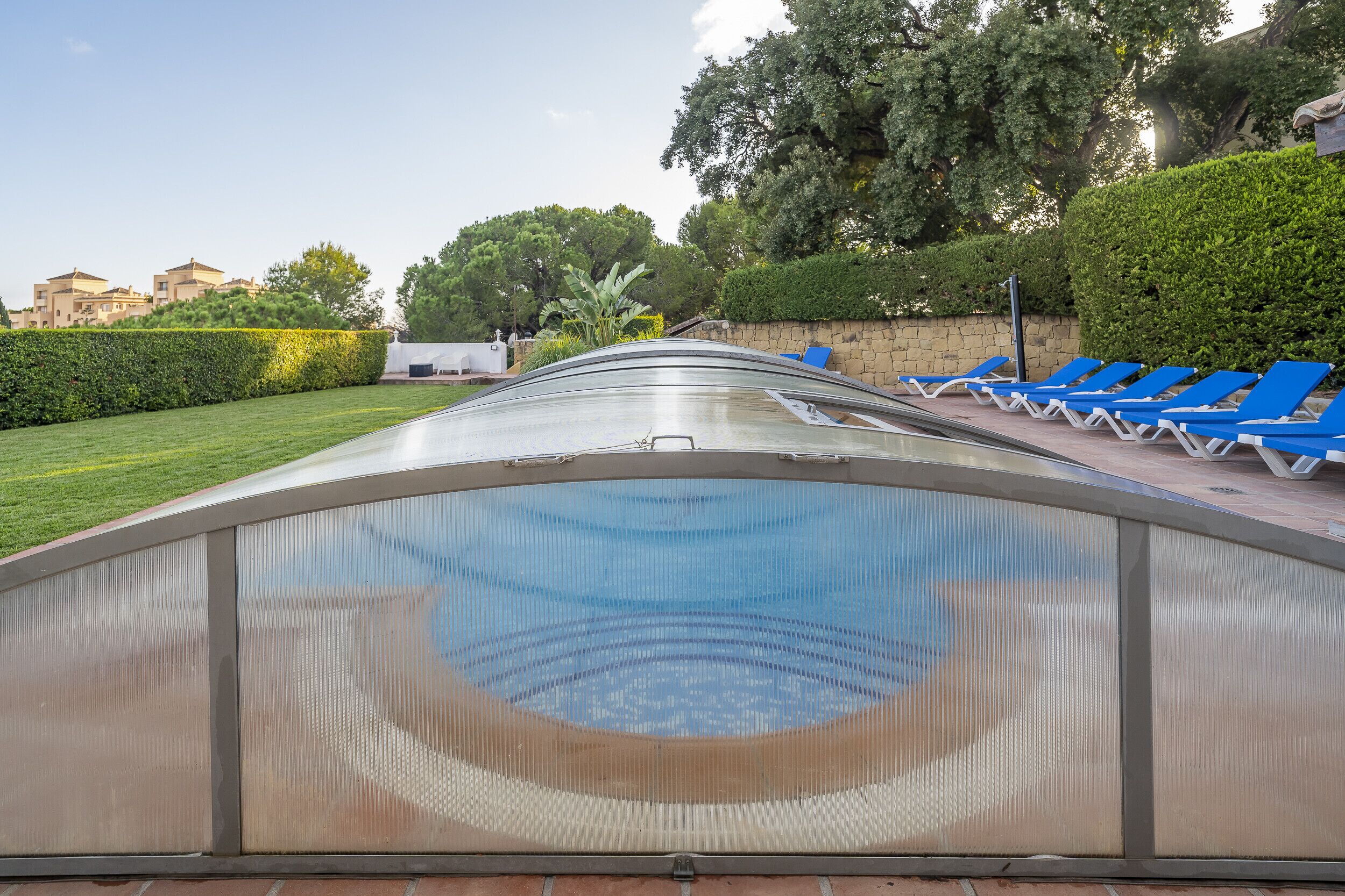 Una piscina exterior con sillones reclinables azules y vistas despejadas de la vegetación y los edificios circundantes.