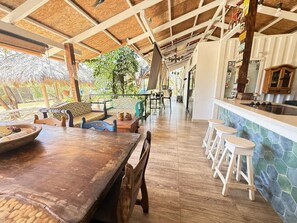 Enjoy meals at the rustic dining table, surrounded by a bar area and a large window offering a view of the outdoors.