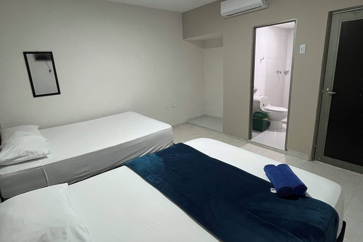A hotel room with two beds, a bathroom visible through an open door, and an air conditioning unit on the wall.