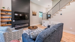 Ein modernes Wohnzimmer mit Kamin, Flachbildfernseher und einer Treppe.