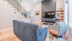 A modern living room with a staircase, a flat-screen TV, and a fireplace. - Woodside Retreat-A: Modern Home (Scottsville)