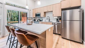 A modern kitchen with wooden cabinets, stainless steel appliances, and a large island with bar stools. - Woodside Retreat-A: Modern Home (Scottsville)