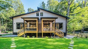 A modern two-story house with a wooden deck and a staircase leading to the entrance. - Woodside Retreat-A: Modern Home (Scottsville)