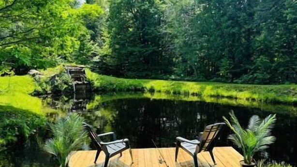 A wooden deck with two chairs overlooking a pond surrounded by lush greenery.