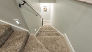 A carpeted staircase with a handrail, white walls, and a poster on the wall. - Pleasant Stay Place - New Build/Zion/Sand Hollow (Hurricane)