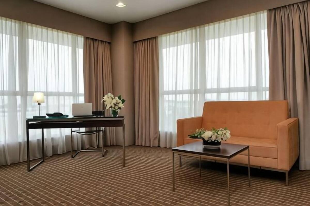A hotel room with a sofa, a desk with a lamp, and a flower arrangement.