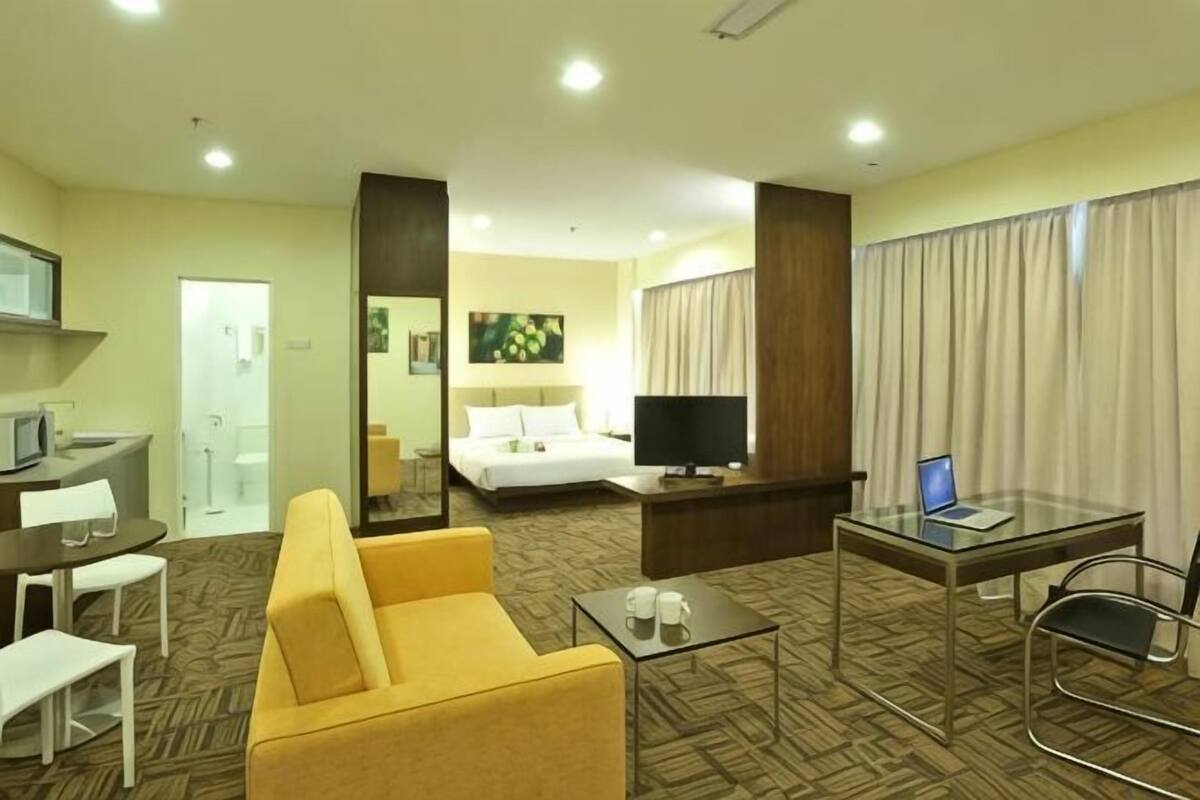 A hotel room with a bed, a desk with a computer, a sofa, a TV, and a glass table.