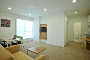 A modern living room with a sofa, coffee table, and a TV on a wall. There is a dining area with a table and chairs, and a kitchen area with a counter and cabinets. - Hotel Primera Suite Cyberjaya (Cyberjaya)
