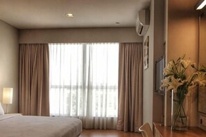 A hotel room with a large bed, a desk, a chair, a vase with flowers, and a window with curtains. - Hotel Primera Suite Cyberjaya (Cyberjaya)