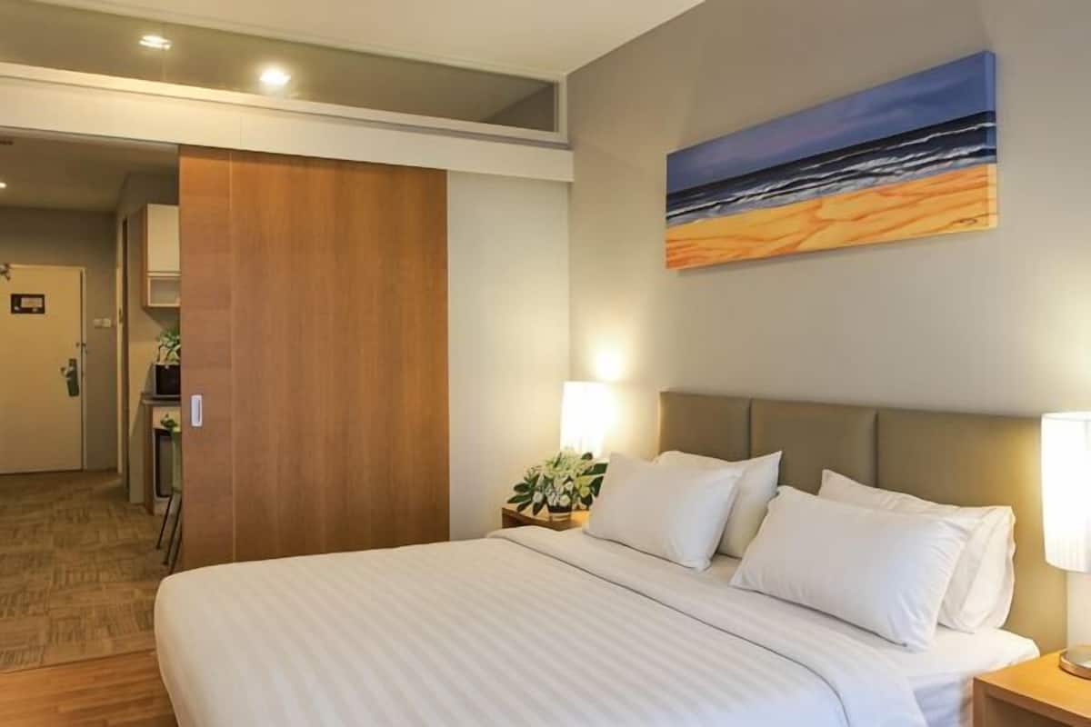 A hotel room with a bed, a nightstand, a painting, and a door leading to a bathroom.