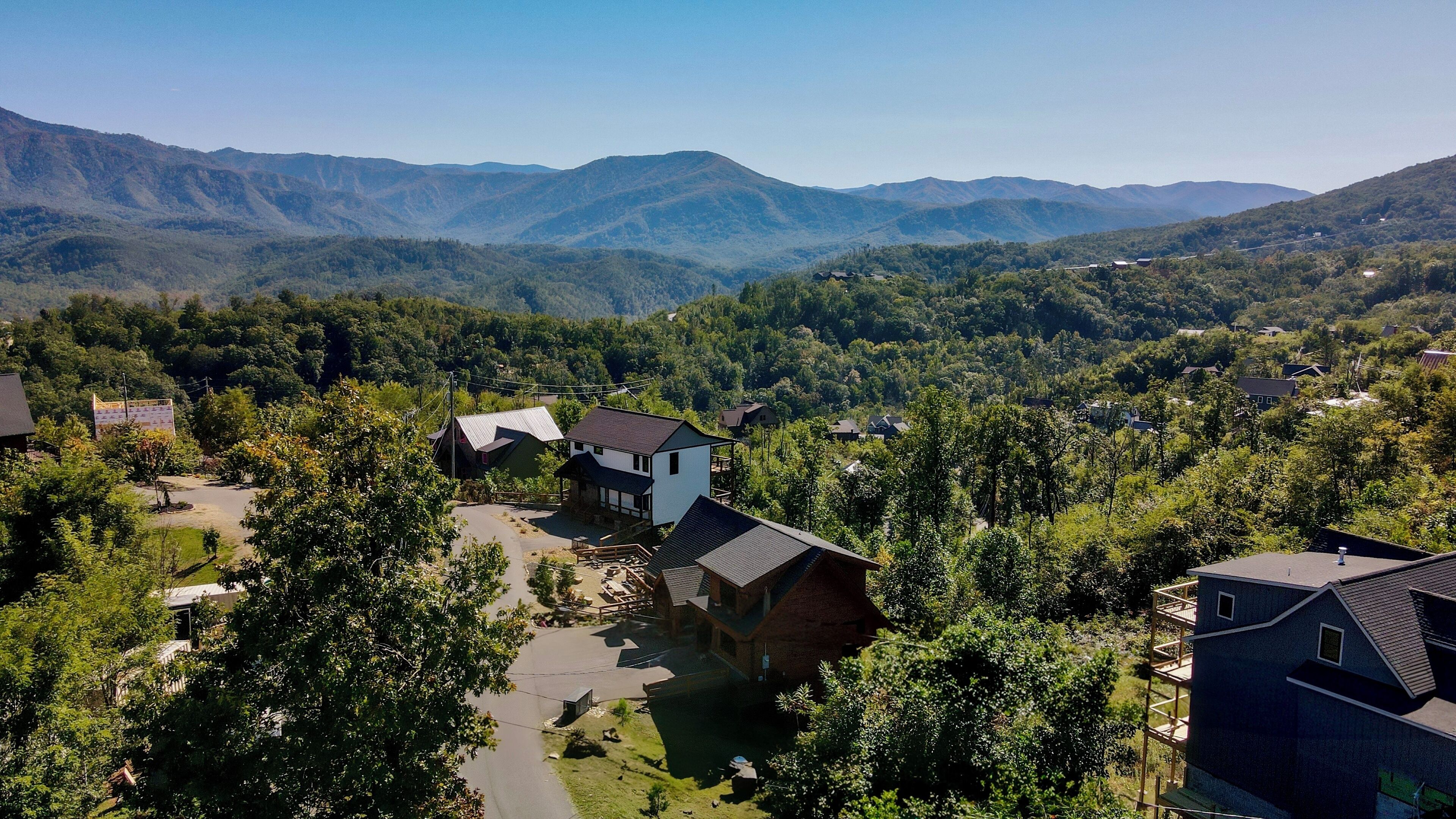 A residential area with houses surrounded by lush greenery and mountains in the background.