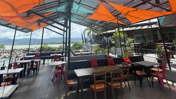 An outdoor seating area with tables and chairs, covered by large umbrellas, overlooking a body of water. - Tubotel Langkawi (Langkawi)