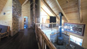 Ein Holzblockhaus im Inneren mit Schlafzimmer im oberen Bereich, einem Kamin aus Stein und einer Holztreppe.