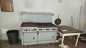 A kitchen with a stove, a trash can, and a table.