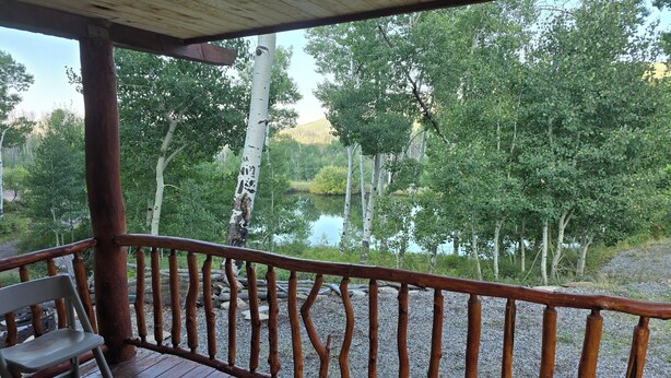 Um deck de madeira com guarda-corpo, com vista para um lago rodeado por árvores.