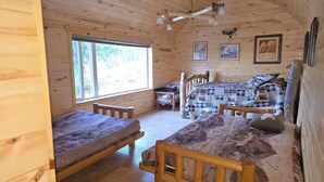 Um quarto de cabana acolhedor com duas camas de madeira, uma janela grande e um ventilador de teto.