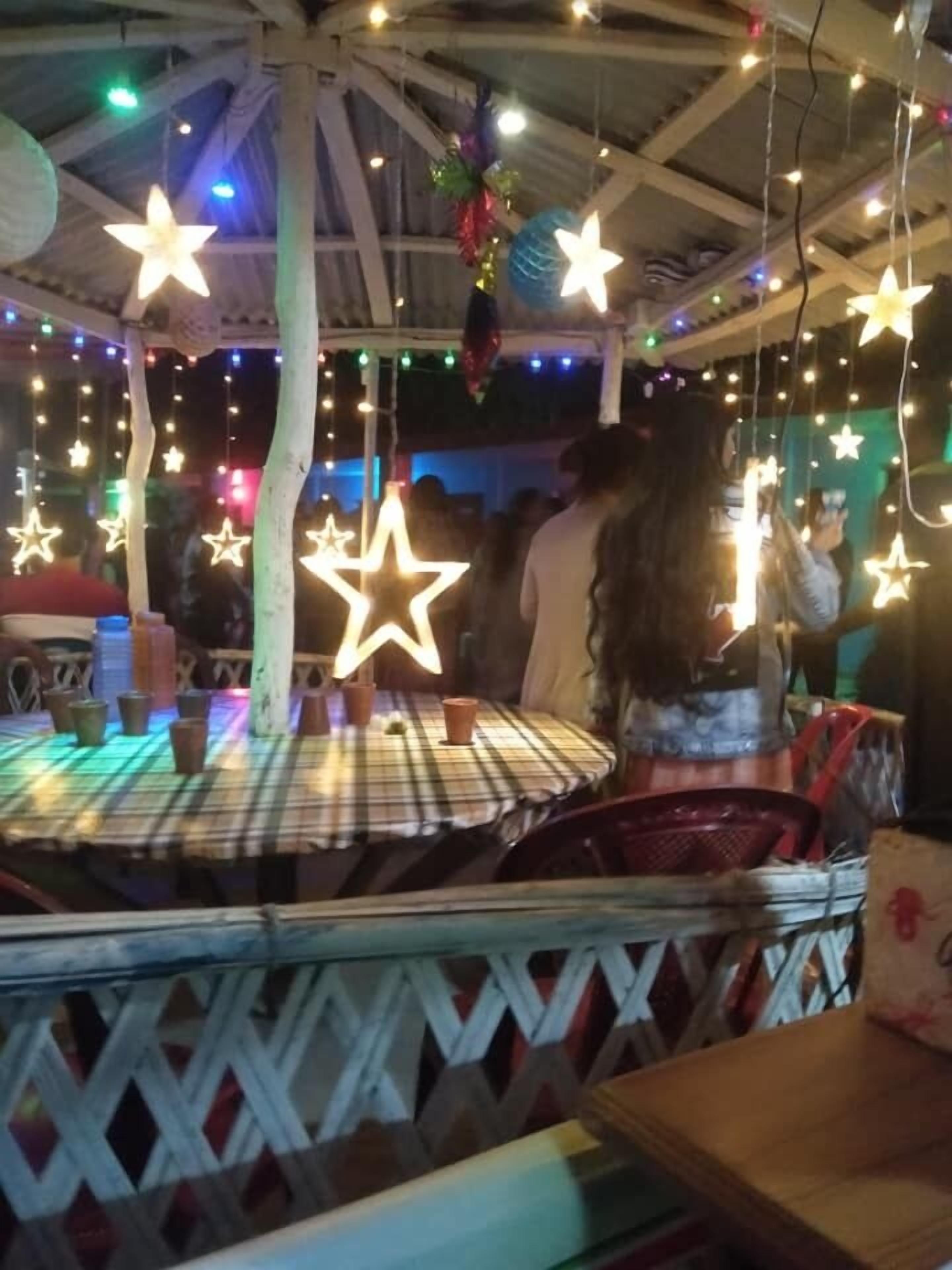 Uma área de estar coberta ao ar livre, com mesas e cadeiras, decorada com luzes em formato de estrela penduradas.