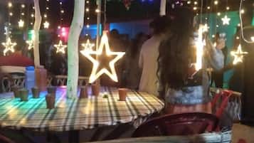 Uma área de estar coberta ao ar livre, com mesas e cadeiras, decorada com luzes em formato de estrela penduradas.