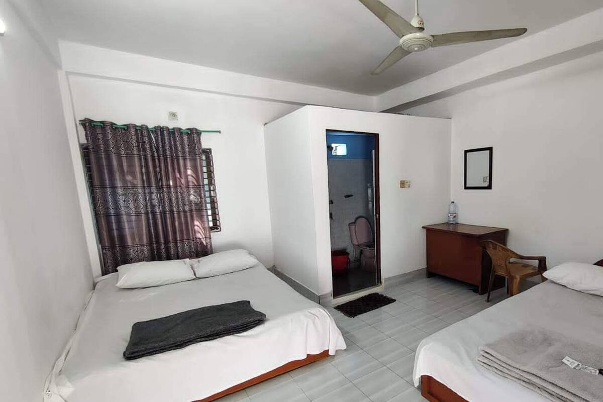 Ein Hotelzimmer mit zwei Betten, einem Schreibtisch, einem Stuhl, einem Kleiderschrank und einem Deckenventilator.