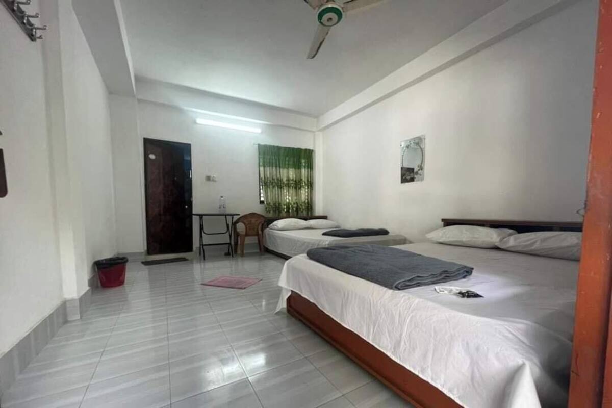 Ein Hotelzimmer mit zwei Betten, einem Deckenventilator, einem kleinen Tisch und einem Stuhl.