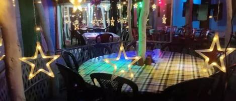 An outdoor seating area with tables and chairs, decorated with star-shaped lights and colorful string lights.
