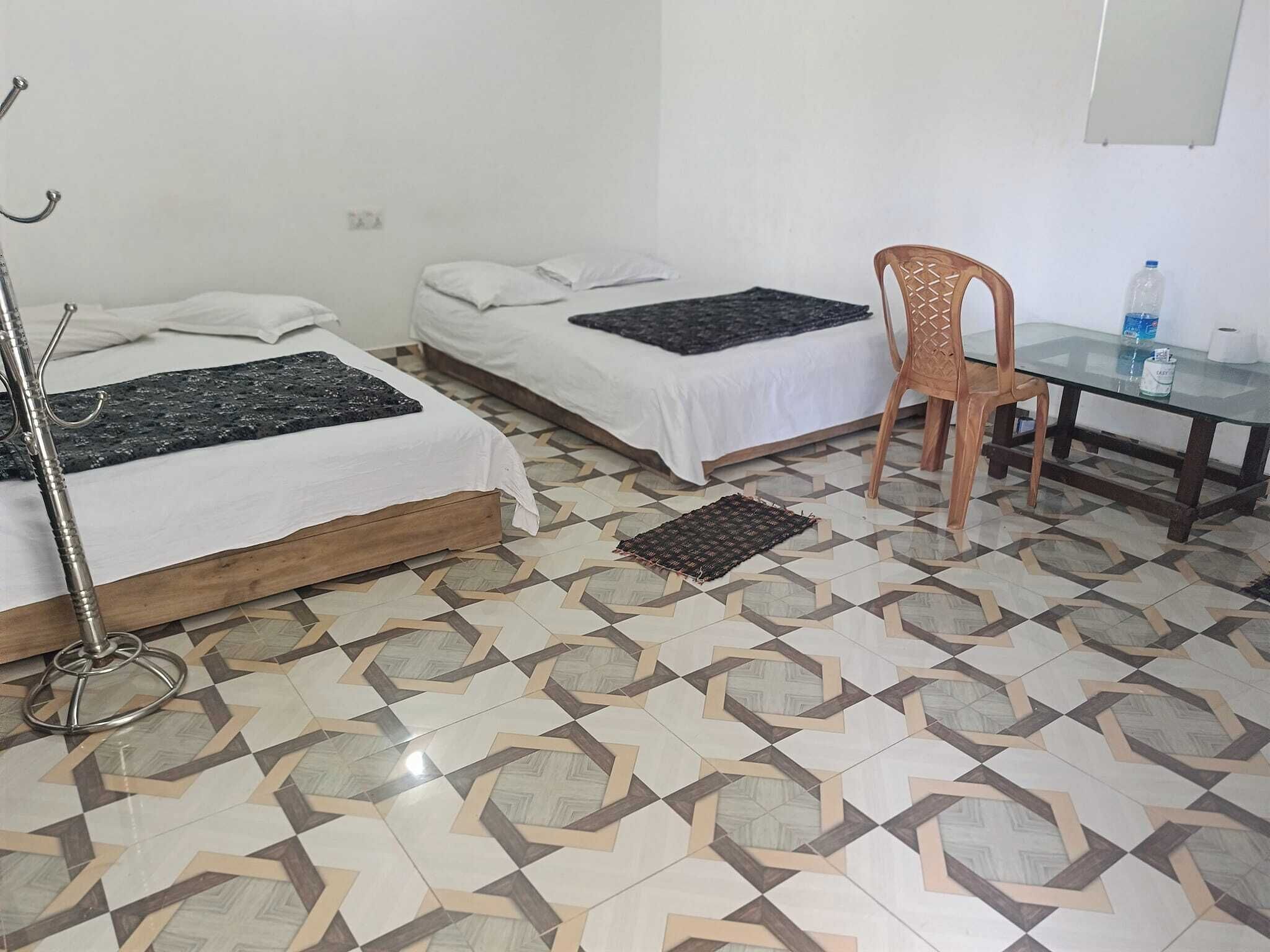 Una habitación con dos camas, una silla, una mesa y un piso con un diseño geométrico de azulejos.