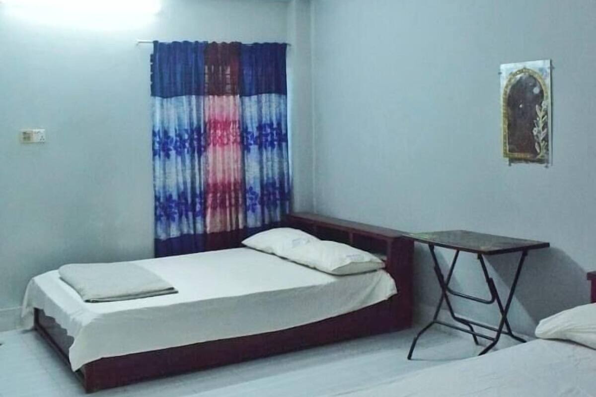 Ein Zimmer mit zwei Betten, einem kleinen Tisch und einem Vorhang.
