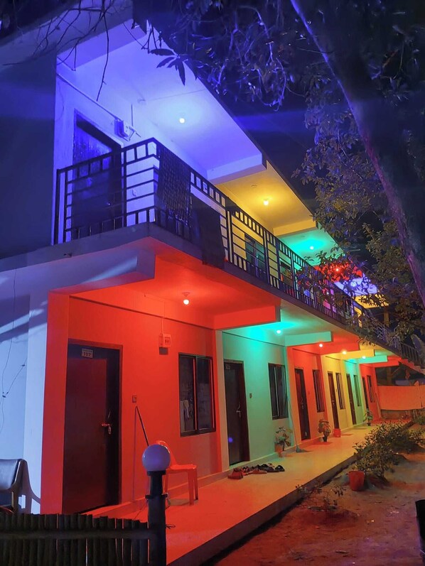 A two-story building with a balcony on the upper floor, a covered outdoor area, and a small garden.